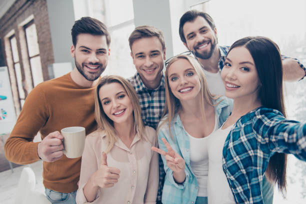 istock Self portrait of cheerful, joyful, positive students managers shooting selfie on front camera in modern office showing two fingers, like, peace, hi sign, holding cup with coffee, partnership 964962384