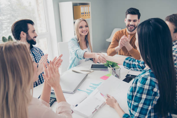 istock Attractive, stylish, confident business people sitting at desktop having conference, gathering, two beautiful girls shaking hands, their cheerful, glad, positive, cheerful colleagues clapping hands 964972276