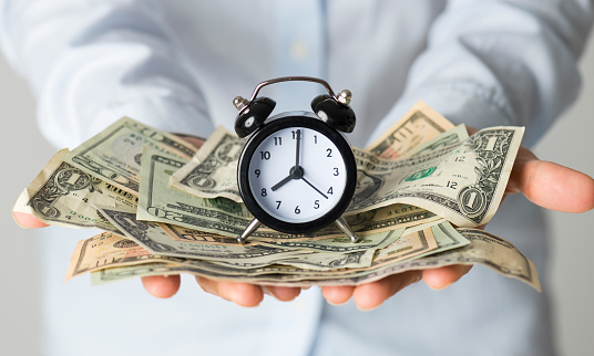 Woman holding paper currency and alarm clock.