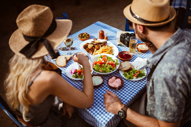 Young tourists couple eating traditional Greek food at rustic restaurant Tourists on Mediterranean summer holidays having lunch and eating traditional meze at rustic tavern greek food stock pictures, royalty-free photos & images