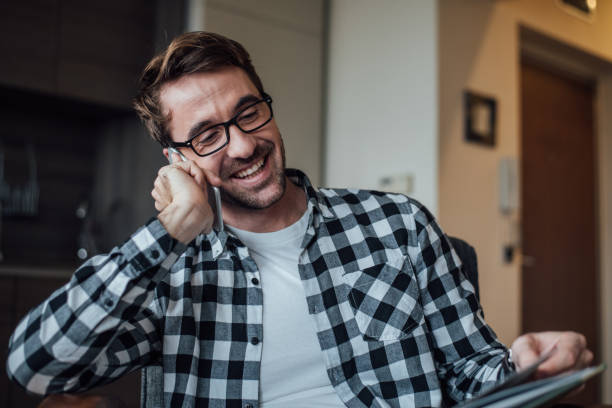 istock Young man reading a book and using mobile phone at home 964990812
