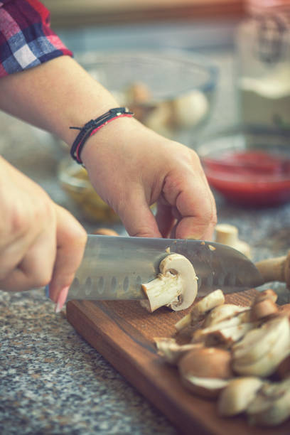 Young woman preparing ingredients for pizza at home, she chopping mushrooms on a cutting board