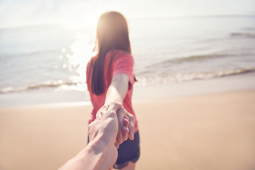 Happy couple on the beach, summer vacations or honeymoon, woman holding hand of husband following her.