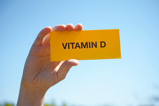 Hand holds piece of paper with Vitamin D against sunny blue sky. Close up.