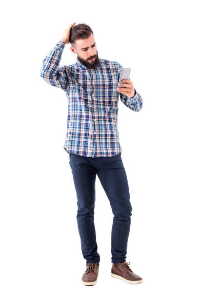 Worried young man touching head reading news on mobile phone. Full body isolated on white background.