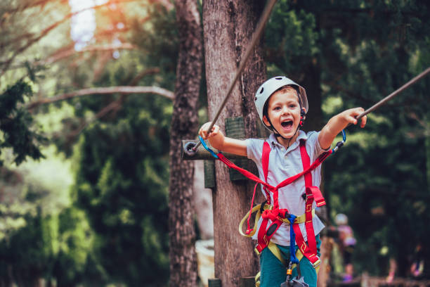 Happy boy playing at adventure park on sunny day. Little boy climbing in adventure activity park with helmet and safety equipment zip line stock pictures, royalty-free photos & images