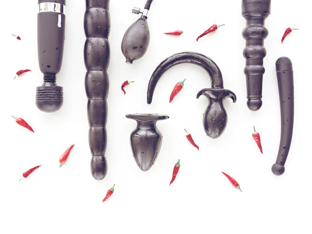 Various wet sex toys with drops of water on them and small red hot peppers are on a white background. stock photo