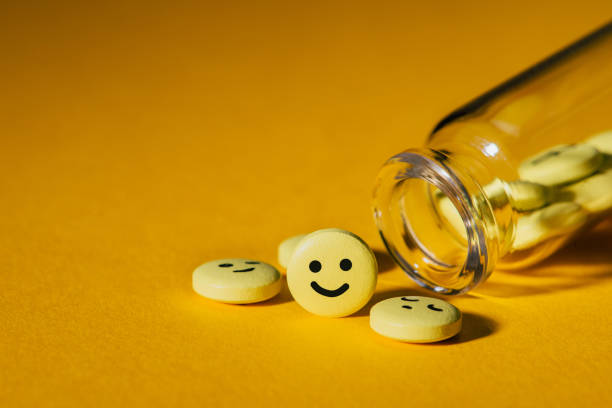close-up shot of pills with smiley faces and glass bottle on yellow - ecstasy imagens e fotografias de stock