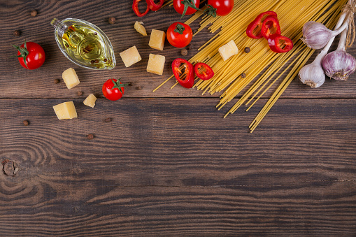 Italian food cooking concept. Ingredients for preparation spaghetti - raw pasta, cherry tomato, olive oil, garlic, cheese, spices, dark wooden background. Pasta background. Top view with copy space