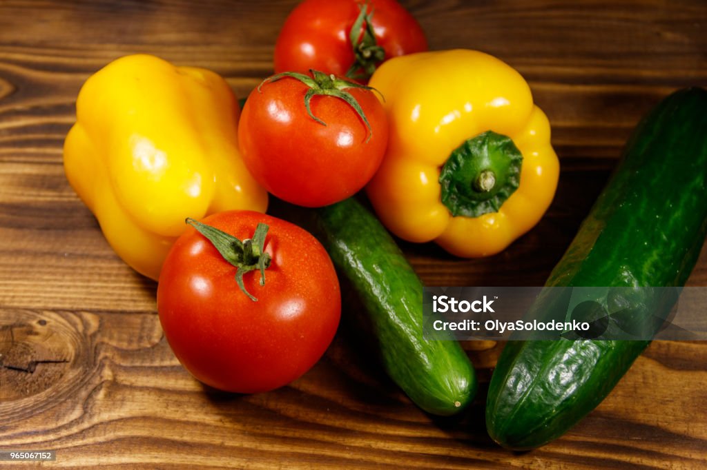 Heap of fresh vegetables on the kitchen table Heap of fresh vegetables on the kitchen table. Ripe tomatoes, peppers and cucumbers on wooden background Agriculture Stock Photo