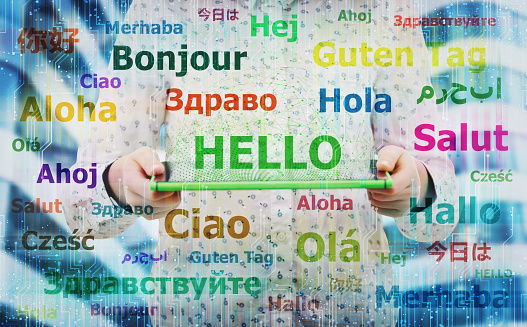 Young woman holding electronic tablet showing the word hello in different languages. Learning and speaking many languages easier using modern technology. International communication concept.