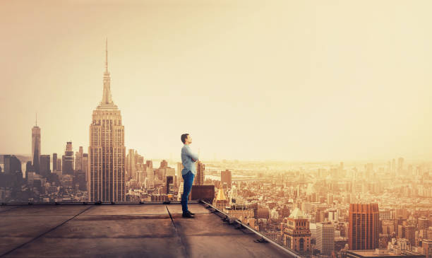 бизнесмен наблюдает за большим городом на закате - men on roof стоковые фото и изображения