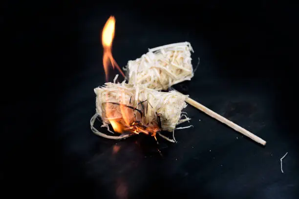 burning wood wool barbecue lighter on a black metal bowl, copy space, selected focus