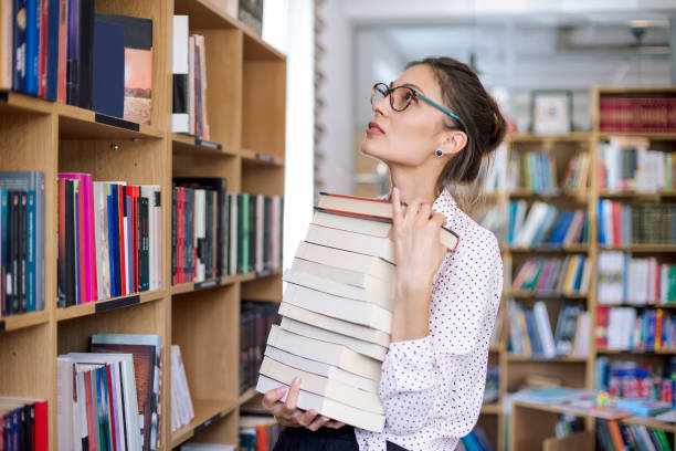 istock Young woman with a stack of books in library 965131890
