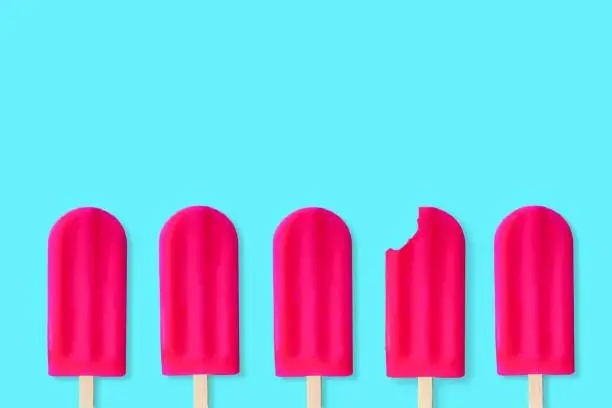 Group of bold pink popsicles on a pastel blue background. One with bite removed.