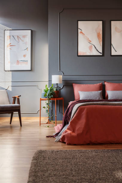 istock Orange bed against dark wall with molding and white posters next to a metal bedside table with a lamp on it in bedroom interior. Real photo 965218400