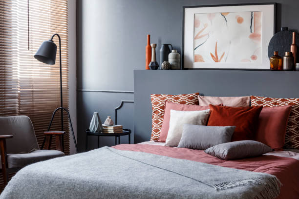 istock Creative poster on black bedhead above cozy bed with decorative cushions and gray blanket in bedroom interior with metal lamp and vintage armchair. Real photo 965218404