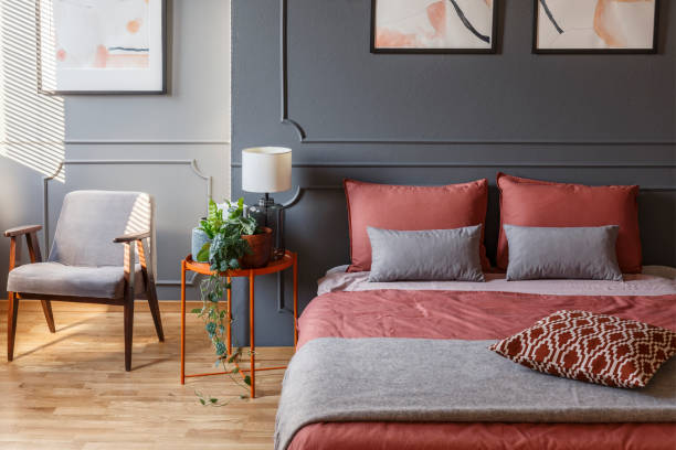 istock Cozy hotel room interior with a double bed with pillows next to a bedside table, plant and armchair 965218410