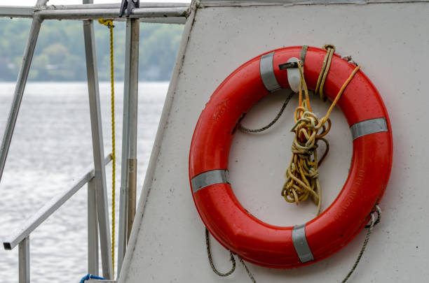 preservatore di vita rosso montato su una barca con acqua e litorale sullo sfondo. - life jacket life belt buoy float foto e immagini stock