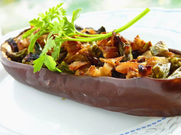 Close up image of stuffed aubergine on a white plate. Halved eggplant stuffed with mushrooms, vegetables and cheese. stock photo