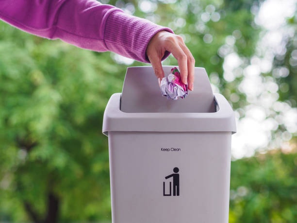istock female hand trowing a paper into a garbage bin on bokeh background. cleaning concept. 965331408