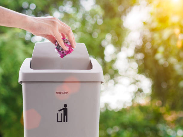 istock female hand trowing a paper into a garbage bin on bokeh background. cleaning concept. 965331412