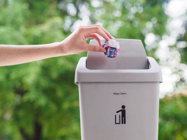 istock female hand trowing a paper into a garbage bin on bokeh background. cleaning concept. 965331414
