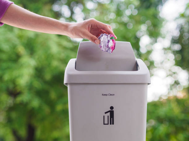 istock female hand trowing a paper into a garbage bin on bokeh background. cleaning concept. 965331592