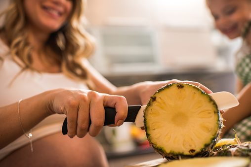 Close up of a woman cutting pineapple in the kitchen.