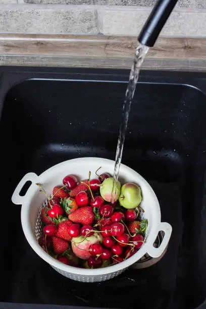 Ripe Fresh Berries and Fruits in black kitchen-sink under stream water. Summer Food Concept