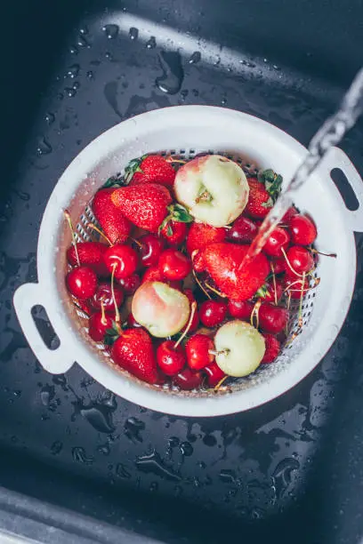 Ripe Fresh Berries and Fruits in black kitchen-sink under stream water. Summer Food Concept