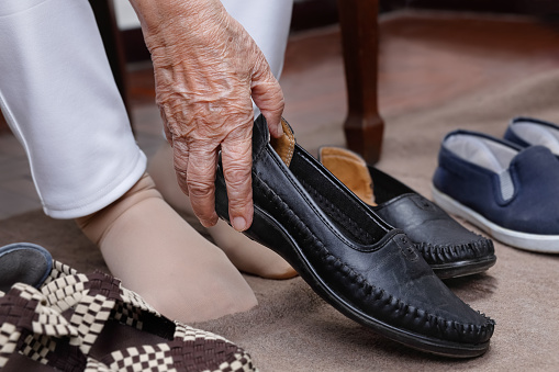 Elderly woman swollen feet putting on shoes at home.