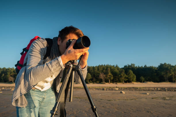 istock Professional photographer on location and making photo standing with tripod on beach 965366162