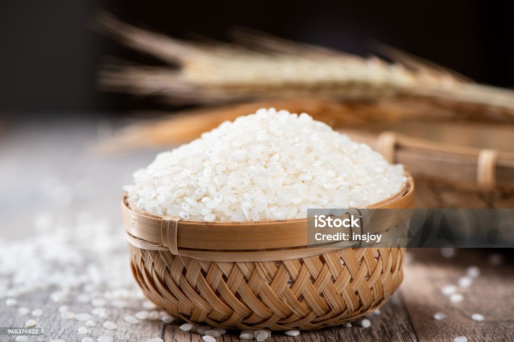 raw rice in a bamboo basket with wheat on wooden background Basket Stock Photo