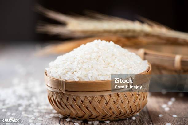 Raw Rice In A Bamboo Basket With Wheat On Wooden Background Stock Photo - Download Image Now