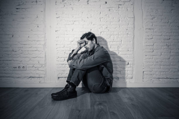 istock young depressed man sitting against a white wall at home with a shadow on the wall feeling miserable, lonely and sad in mental health depression concept 965384304