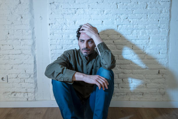istock young depressed man sitting against a white wall at home with a shadow on the wall feeling miserable, lonely and sad in mental health depression concept 965384362