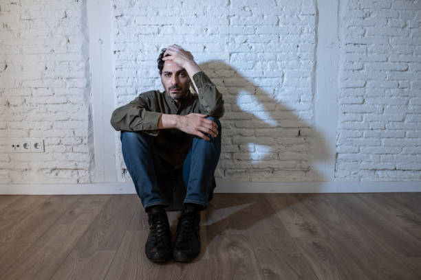istock young depressed man sitting against a white wall at home with a shadow on the wall feeling miserable, lonely and sad in mental health depression concept 965384376