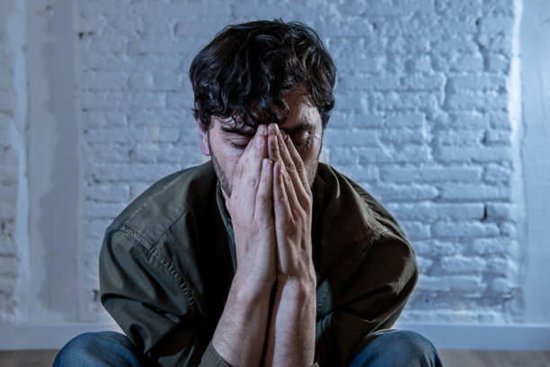 istock young depressed man sitting against a white wall at home with a shadow on the wall feeling miserable, lonely and sad in mental health depression concept 965384434