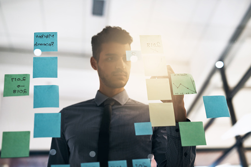 Cropped shot of a young businessman brainstorming on a glass wipe board in a modern office