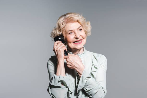 グレーに分離されたヴィンテージの電話で話し笑顔のシニア女性のクローズ アップの肖像画 - landline phone women close up old fashioned ストックフォトと画像