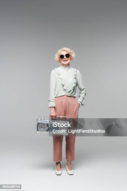 Beautiful Senior Woman In Stylish Sunglasses With Vintage Boombox On Grey Stock Photo - Download Image Now