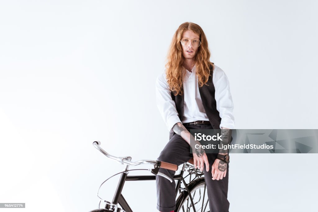 stylish tattooed businessman with long ginger hair sitting on bicycle isolated on white Adult Stock Photo