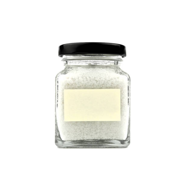 istock Salt in a glass bottle isolated on white background. Empty yellow stick note paper and black lid. Modern and stylish. Close up. 965415478
