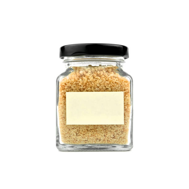 istock Brown sugar in a glass bottle isolated on white background. Granulated sugar. Empty yellow stick note paper and black lid. Modern and stylish. Close up. 965415806