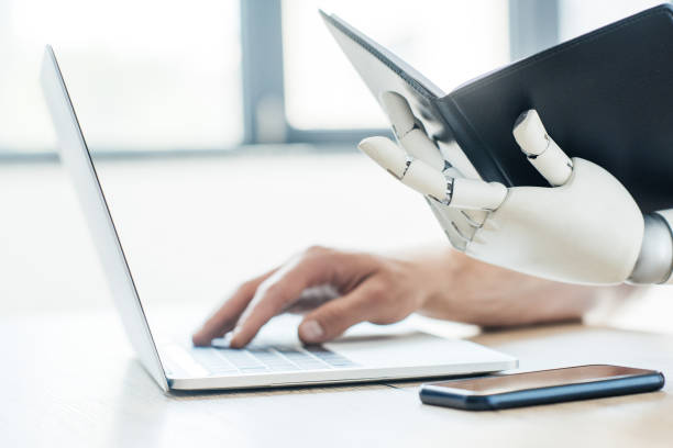 istock close-up view of robotic arm holding notebook and human hand using laptop at workplace 965424046