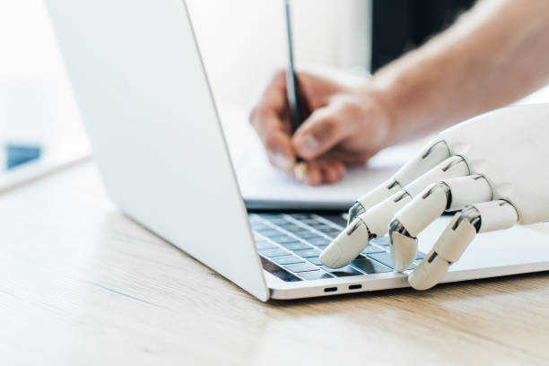 istock close-up view of robotic arm using laptop and human hand taking notes at wooden table 965424270