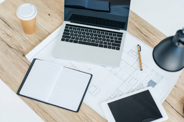 istock high angle view of laptop, digital tablet, notebook and blueprint on wooden table 965425110