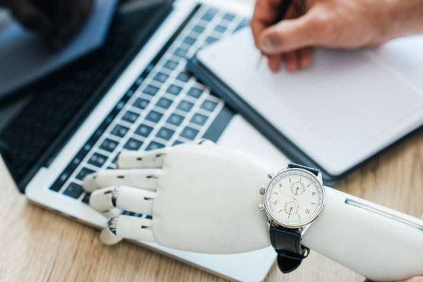 istock selective focus of robotic arm with wristwatch using laptop and human hand taking notes at wooden table 965425334