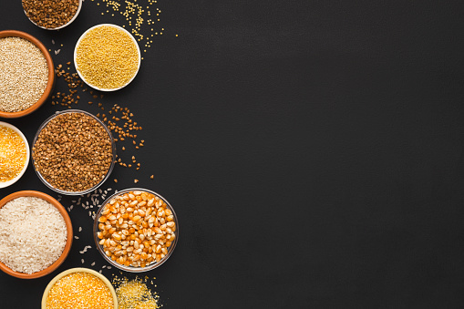 Border of assorted gluten free grains in bowls on black background, copy space, top view